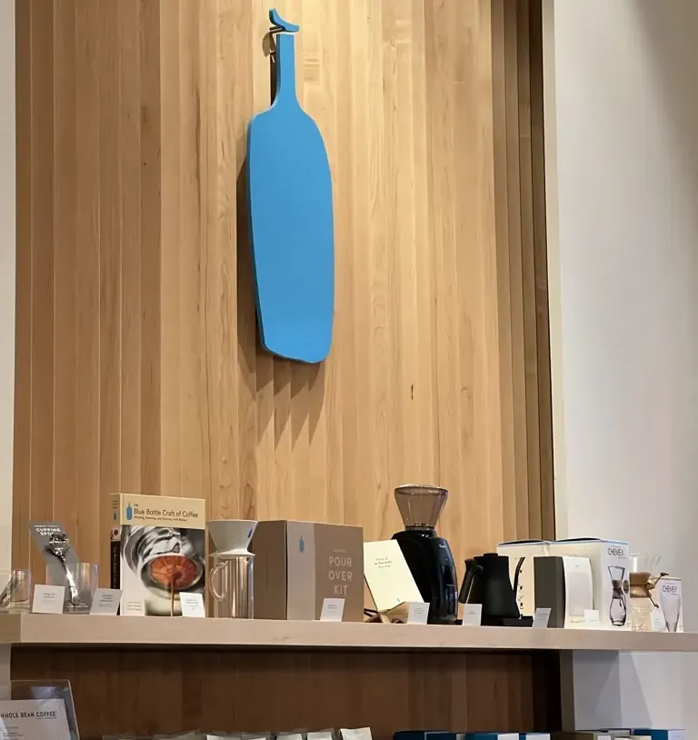 Prateleira da Blue Bottle Coffee, com o logo da garrafa azul e kits de coado